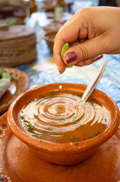 Squeezing lime juice into traditional Mexican soup in clay bowl