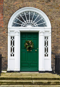 Green Georgian front door decorated for Christmas Holiday season with seasonal wreath. Entrance to house with decorative fanlight and columns. Dublin, Ireland