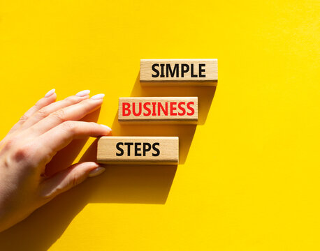  Concept words simple business steps on wooden blocks arranged as steps. Business planning concept. Businessman hand arranging wooden blocks. Yellow background. Copy space.