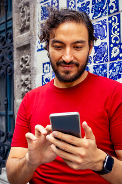 Close up of hispanic young man using smartphone leaning against traditional Talavera tile wall