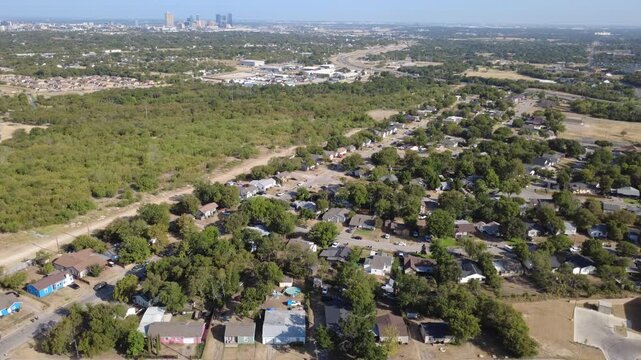 Dense shade trees envelop single-story residential properties across historic Morningside. Unpaved access paths trace natural woodland edges beneath sunny clear skies, Fort Worth, Texas