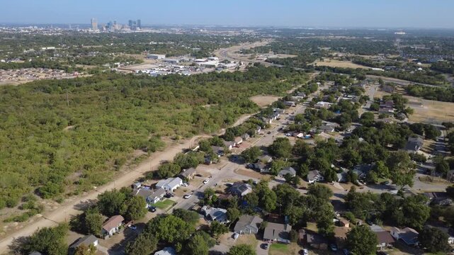 Sprawling tree canopies border quiet single-family subdivisions across DFW Metroplex. Distant downtown skyline towers rise above verdant green nature preserves under sun, Fort Worth, Texas