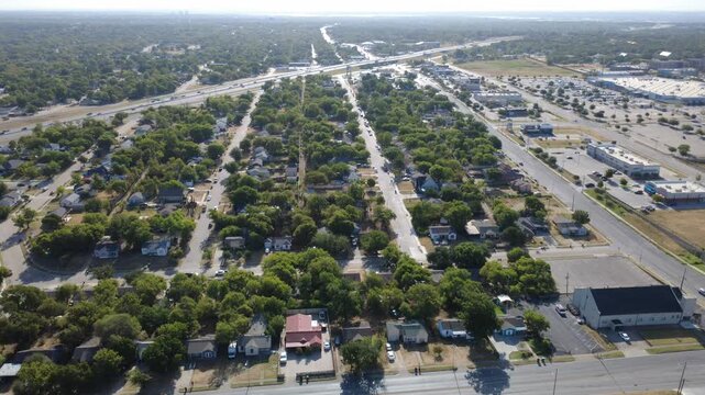 Linear neighborhood avenues cut through mature tree canopies across DFW Metroplex. Quiet residential suburban properties border expansive paved commercial parking spaces, Fort Worth, Texas