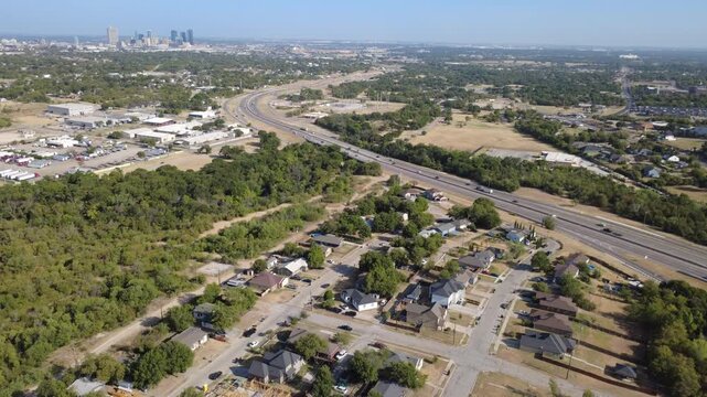 Active home construction frames rising timber framing near US-287 across DFW Metroplex. Sweeping expressway corridors lead toward distant downtown skyline silhouettes, Fort Worth, Texas