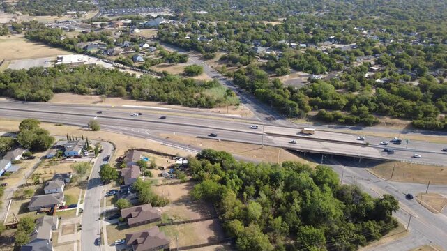 Multi-lane concrete overpass carries US-287 traffic directly across historic Morningside. Single-family homes nestle beside lush green tree canopies beneath bright skies, Fort Worth, Texas