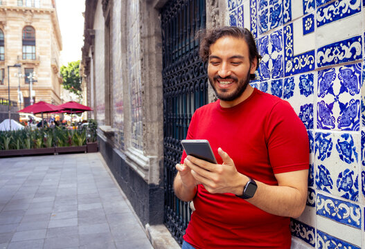 Young man using smartphone leaning against traditional Talavera tile wall in Mexico City