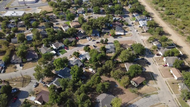 Paved suburban avenues intersect quiet residential blocks across Tarrant County. Mature shade trees surround single-story rooftops beside private paved driveways, Fort Worth, Texas