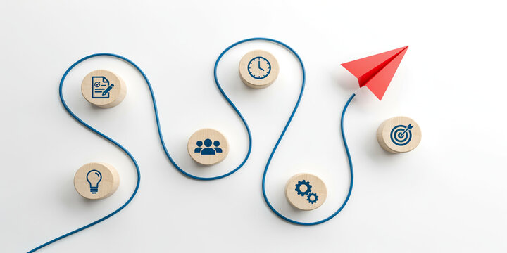 Red paper airplane flying on winding path connected with wooden blocks containing business icons. Corporate process, startup launch, project planning, and strategy development concept.