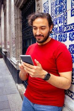 Young man using smartphone leaning against traditional Talavera tile wall