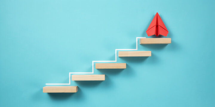 Red paper airplane on top of wooden block stairs with rising step line. Business career progress, startup launch, leadership, and success concept.