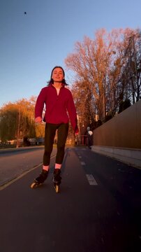 Female skater rollerblades outdoors in warm evening sunlight. Vertical stock clip with smooth movement, casual exercise, and scenic golden hour background