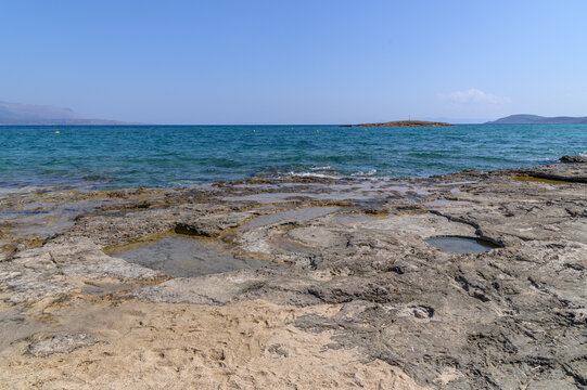 Water-filled basins cut into the flat limestone shore at Pounta with the sea and a low islet beyond, Laconia, Greece