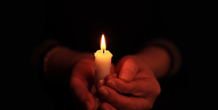 Hands holding burning Candle in dark. Selective soft focus close-up blur smoke black, red, yellow background.