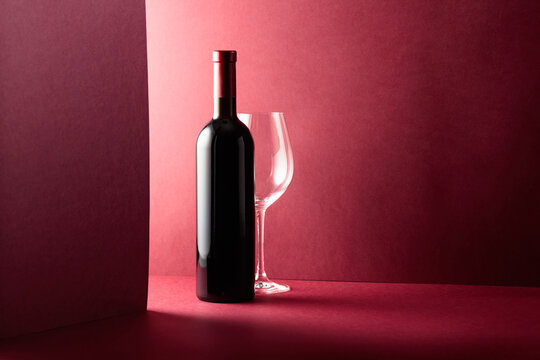Bottle and glass of red wine on a red background.
