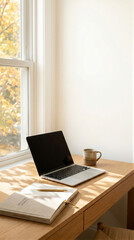 Fototapeta premium Laptop, notebook, pen, and coffee on a wooden desk beside a sunlit window. Minimal home office workspace for remote work, planning, productivity, and business communication
