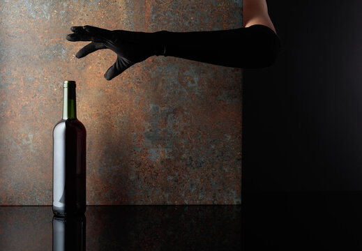 Woman hand in  glove reaches for a bottle of red wine.
