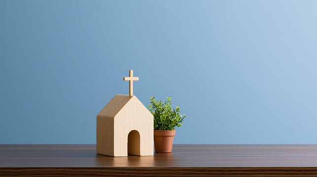 Minimalist wooden church model with a cross on top and a small green plant in a pot on a wooden table against a solid blue background