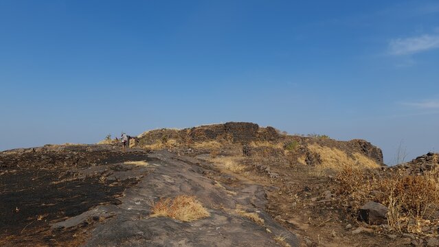 Trekker approaching historic fort ruins on a rocky mountain summit in Maharashtra India