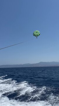 Two people parasailing in the blue sky over the sea, view from the boat