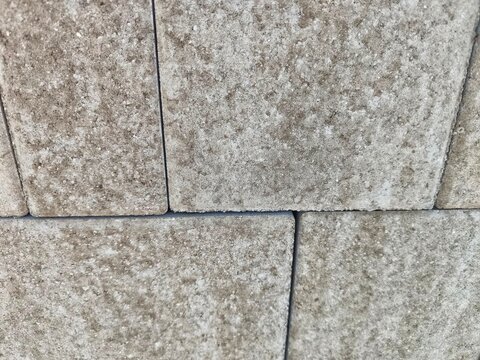 Arrangement of light brown square concrete paving stones with textured stone finish
