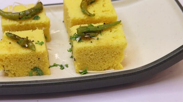Dhokla garnished with green chilli and served on white plate