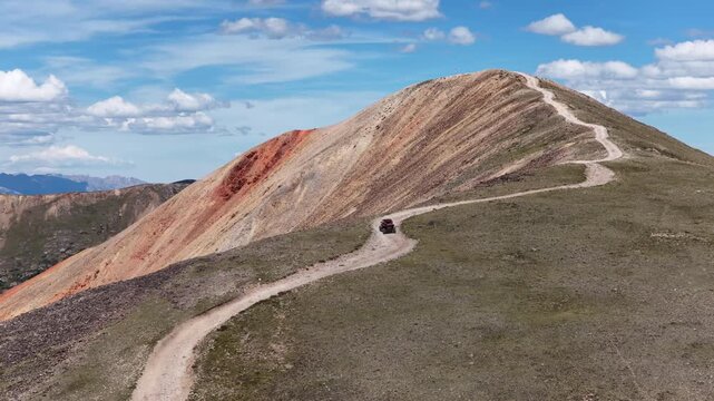 Aerial of UTV side by side vehicle driving Red Cone Peak dirt road in Colorado across red eroded colorful slope at timberline