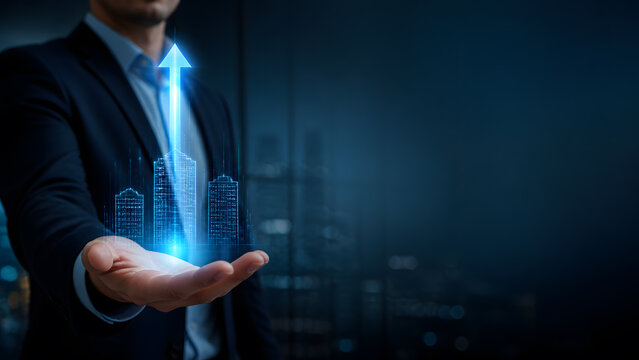 Businessman holding digital hologram of city towers with glowing blue arrow pointing upward for growth