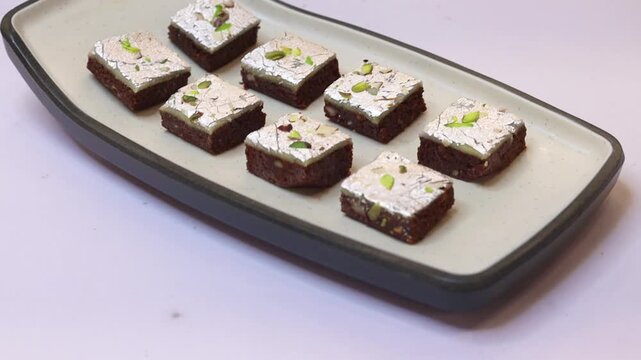 Chocolate barfi or barfee decorated with silver coating and pistachio on a white plate