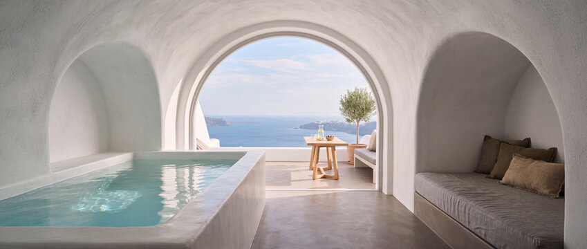 Luxury cave suite with indoor pool overlooking a sunny Mediterranean sea terrace, featuring white arched plaster walls, cozy daybed, and minimalist decor for luxury travel concepts