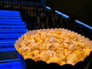 A bucket of popcorn sits on a cinema seat armrest, facing a blank movie screen, with rows of empty theater seats nearby © Татьяна Швец