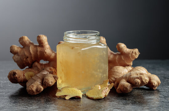 Ginger jam in jar and fresh ginger roots on a black background.