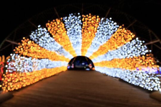 Lights create a colorful arch at a festive event in a park during the evening