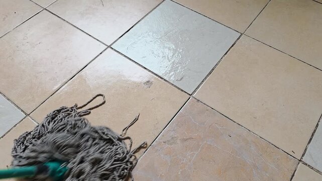 Gray string mop cleans across tiled flooring in a wiping motion, floor cleaning routine