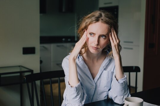 Woman holding both temples while feeling overwhelmed by mental load and stress at home