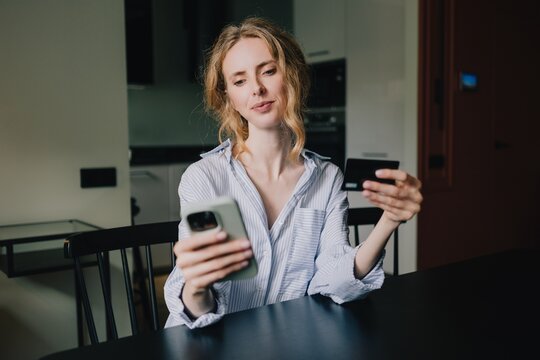 Woman holding a bank card and smartphone while making an online payment at home