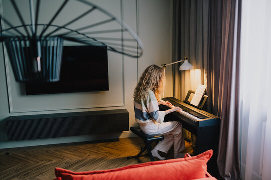Young woman playing digital piano with sheet music in a cozy home music corner