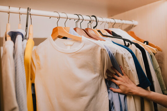 Hand browsing clothes on hangers inside a home wardrobe, choosing between shirts and casual garments while organizing clothing and planning an everyday outfit