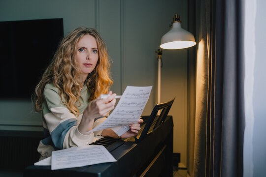 Woman studying sheet music and taking notes at a digital piano at home, focused on musical notation, piano learning and independent music education