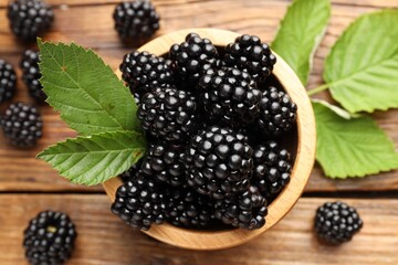 Ripe blackberries in bowl with leaves on wooden table, flat lay © New Africa