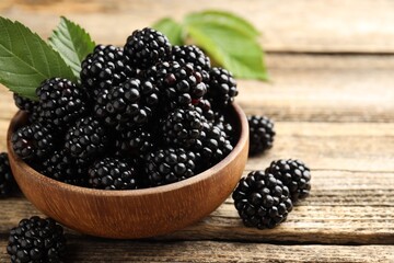 Ripe blackberries in bowl with leaves on wooden table, closeup. Space for text © New Africa