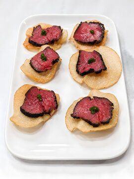 Gourmet Rare Beef Slices Served on Crispy Canap&eacute;s with Green Garnish on White Plate