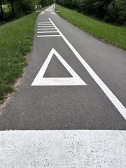 Fototapeta premium Warning triangle road marking painted on an asphalt bicycle path. Cycling infrastructure with safety signs, traffic calming measures and strong leading lines.