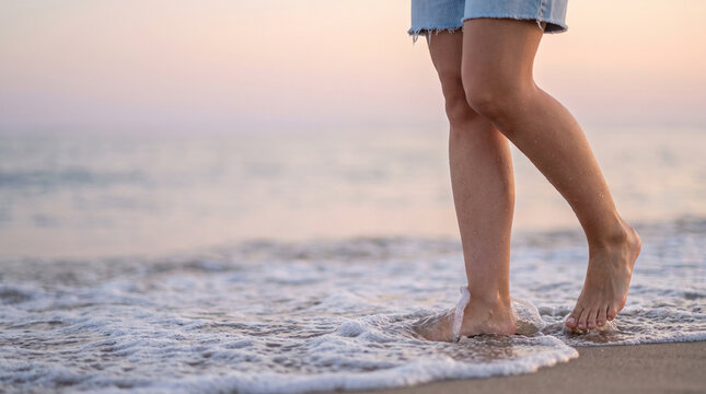 Close Up of Woman Legs Walking Barefoot on Sandy Beach into Ocean Waves at Sunset, Concept of Summer Vacation, Freedom, Wellness, and Relaxation with Left Copy Space for Banner
