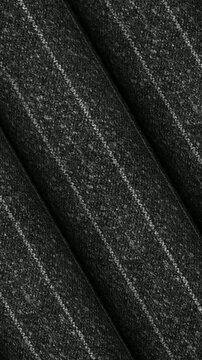 Revolving presentation of Italian dark charcoal gray pinstripe wool fabric rolls displaying subtle line details and elegant business attire material