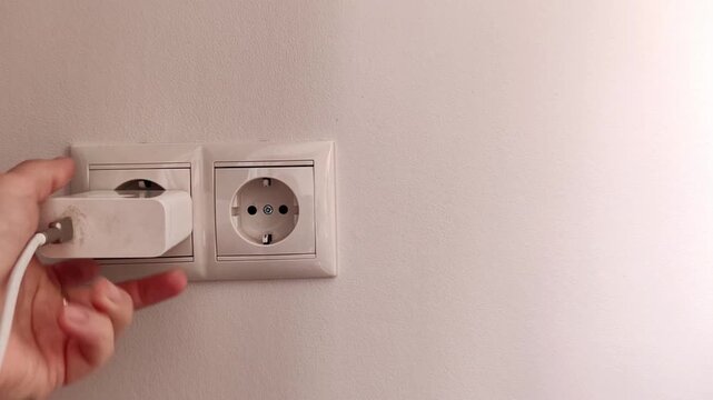 Woman inserts a white electrical plug into a wall outlet, demonstrating household power connection, home maintenance and electrical use