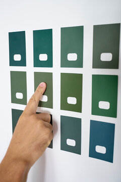 Hand points to one of several green paint color samples on white wall