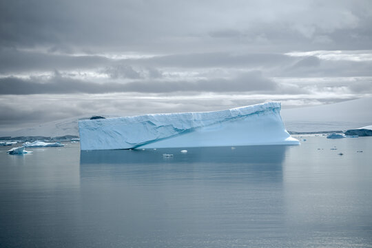 Antarctica: large tabular iceberg floating in the calm waters under a cloudy and gray sky.