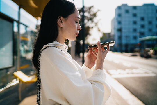 Profile of woman looking at smartphone screen with focus and concentration, checking data, mobile application usage, urban background, digital communication and technology concept.