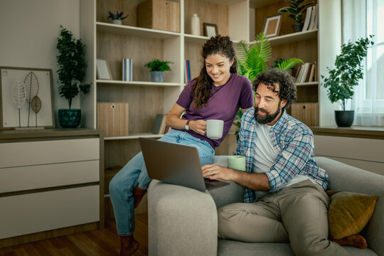 Couple relaxing on couch using laptop and drinking coffee while browsing at home