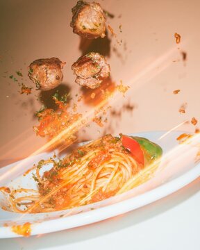 Meatballs falling through the air toward a plate of spaghetti with glossy sauce and fresh herbs, for food packaging and delivery advertising